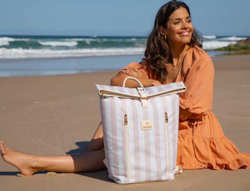 Woman carrying a cooler backpack hands free across the sand on a beach day